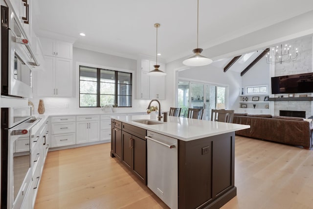 kitchen featuring appliances with stainless steel finishes, sink, white cabinets, hanging light fixtures, and a kitchen island with sink