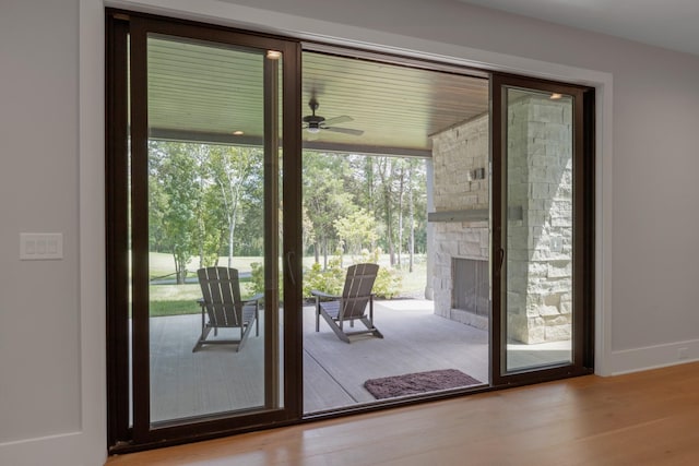 doorway to outside featuring a stone fireplace, light hardwood / wood-style floors, and ceiling fan