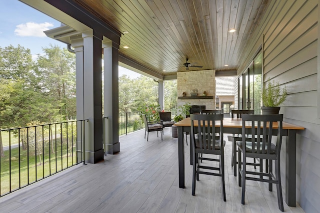 wooden terrace featuring ceiling fan, an outdoor stone fireplace, and a bar