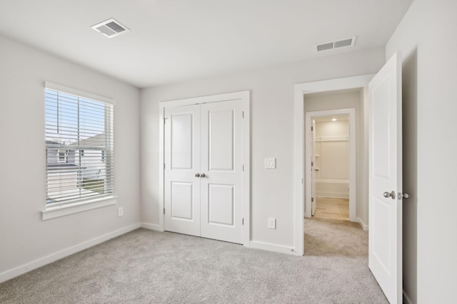 unfurnished bedroom with light carpet, a closet, visible vents, and baseboards