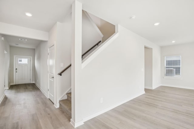 entryway featuring baseboards, light wood finished floors, and stairs