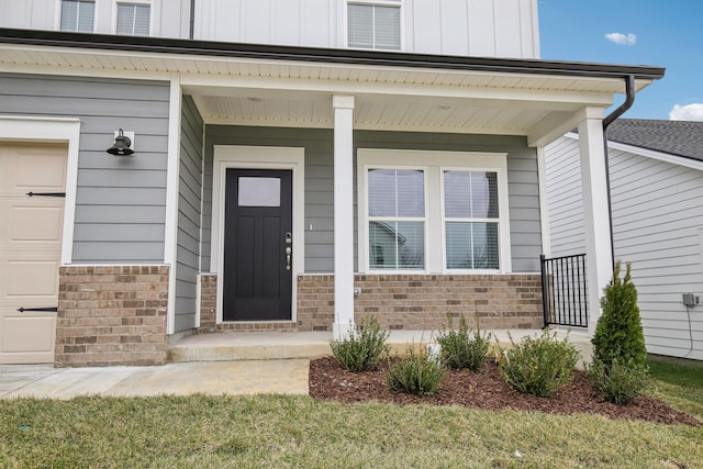 doorway to property with a garage, brick siding, board and batten siding, and a porch