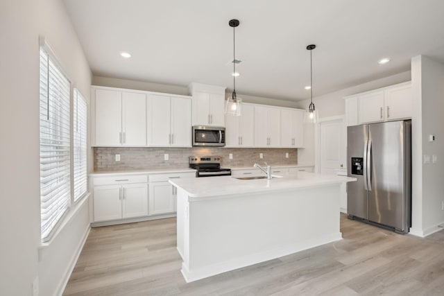 kitchen with stainless steel appliances, white cabinetry, hanging light fixtures, light countertops, and a center island with sink