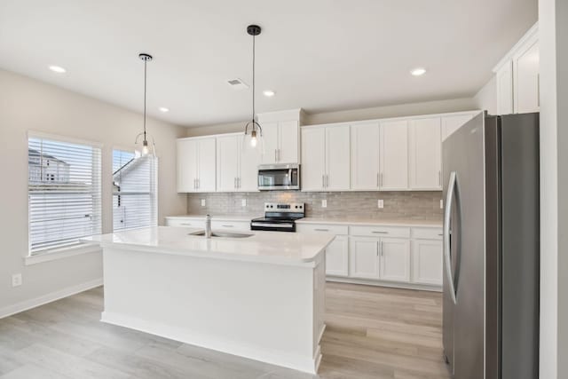 kitchen featuring stainless steel appliances, white cabinetry, light countertops, an island with sink, and pendant lighting