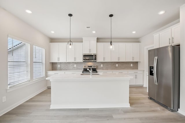 kitchen with a center island with sink, stainless steel appliances, light countertops, hanging light fixtures, and white cabinets