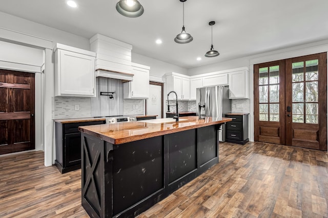 kitchen with sink, white cabinets, hanging light fixtures, a kitchen island with sink, and stainless steel refrigerator with ice dispenser