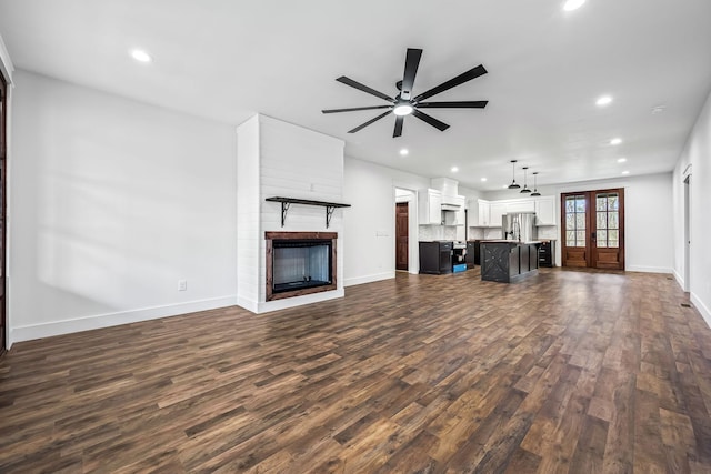 unfurnished living room with dark hardwood / wood-style floors, a large fireplace, ceiling fan, and french doors