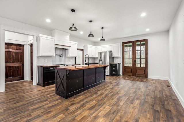 kitchen featuring butcher block countertops, decorative light fixtures, white cabinetry, stainless steel fridge with ice dispenser, and a center island with sink