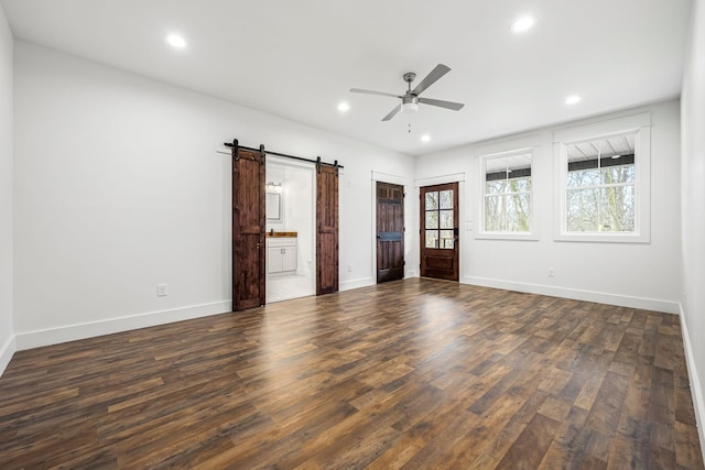 unfurnished bedroom featuring ensuite bathroom, a barn door, dark hardwood / wood-style floors, and ceiling fan