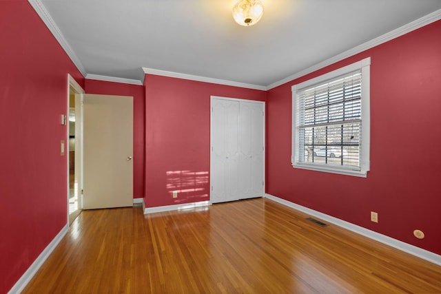 unfurnished bedroom with hardwood / wood-style flooring, crown molding, and a closet