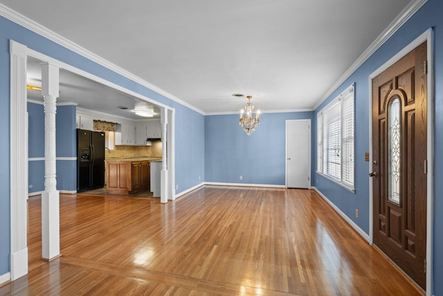 interior space with decorative columns, crown molding, a notable chandelier, and light wood-type flooring