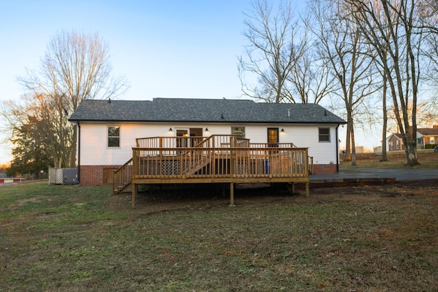 back house at dusk with a wooden deck and a lawn