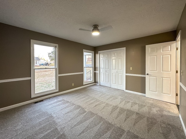 unfurnished bedroom featuring a textured ceiling, a closet, ceiling fan, and carpet