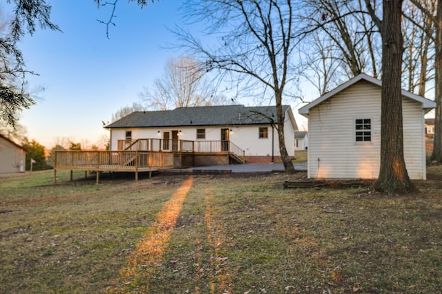 back house at dusk with a wooden deck and a lawn