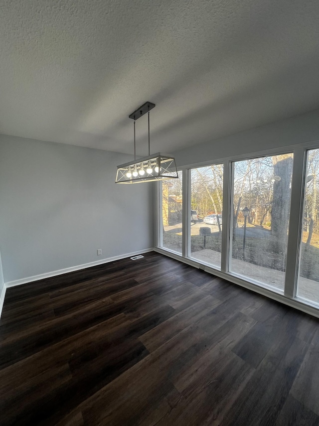 unfurnished dining area featuring dark hardwood / wood-style floors, a textured ceiling, and a wealth of natural light