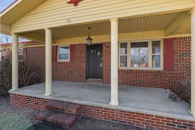 doorway to property with a porch and brick siding