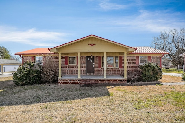 ranch-style house featuring covered porch, metal roof, brick siding, and a front lawn