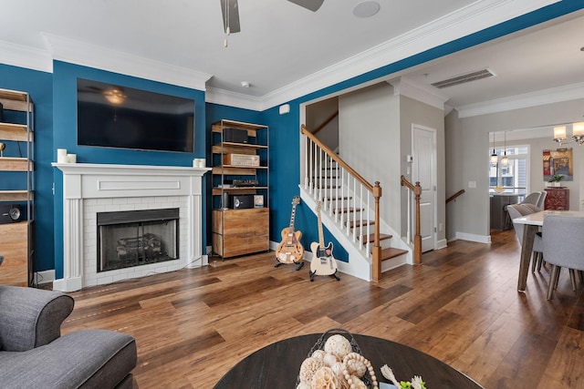 living room featuring ornamental molding, a brick fireplace, wood-type flooring, and ceiling fan with notable chandelier