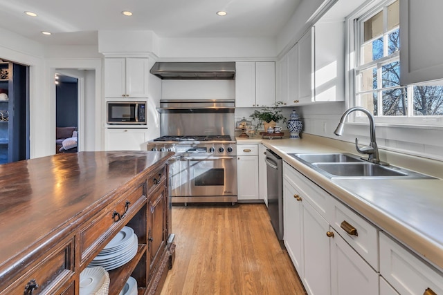 kitchen with white cabinetry, sink, light hardwood / wood-style floors, stainless steel appliances, and wall chimney range hood