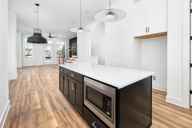 kitchen with white cabinetry, hanging light fixtures, a center island, stainless steel microwave, and light wood-type flooring