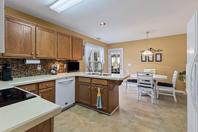 kitchen featuring sink, kitchen peninsula, pendant lighting, white appliances, and backsplash