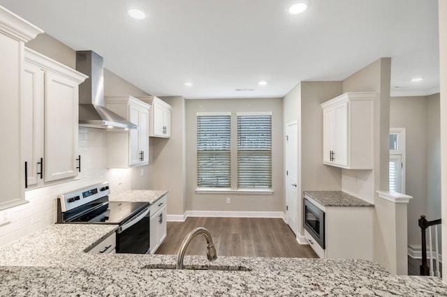 kitchen with light stone counters, white cabinets, stainless steel appliances, and wall chimney exhaust hood