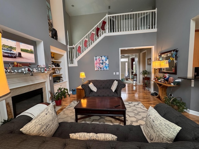 living room featuring a premium fireplace, a towering ceiling, built in features, and light wood-type flooring