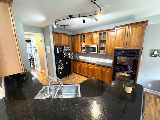 kitchen with sink, hardwood / wood-style flooring, dark stone countertops, tasteful backsplash, and black appliances