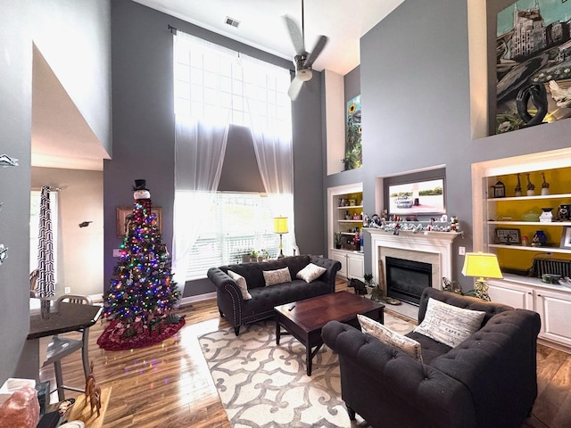 living room with wood-type flooring, built in features, and a high ceiling