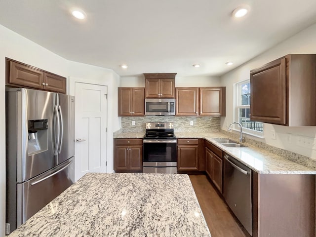 kitchen featuring light stone counters, stainless steel appliances, sink, and backsplash