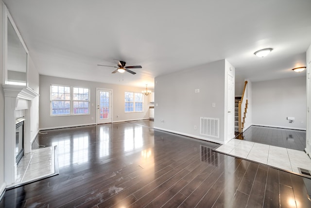 unfurnished living room with dark hardwood / wood-style flooring, ceiling fan with notable chandelier, and a tile fireplace