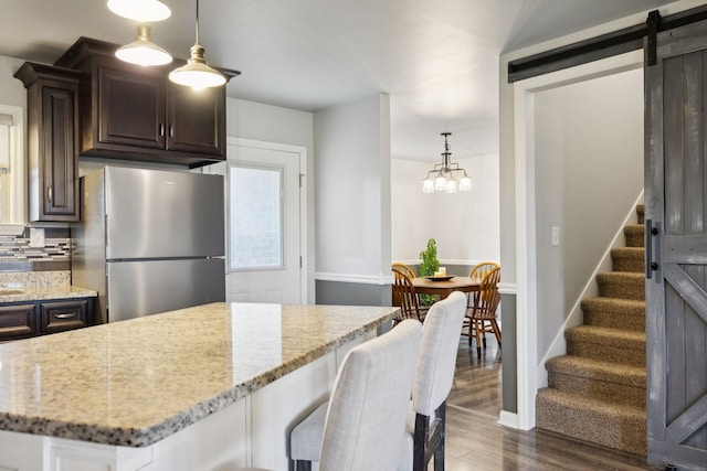 kitchen with dark wood-type flooring, decorative light fixtures, stainless steel fridge, a barn door, and backsplash