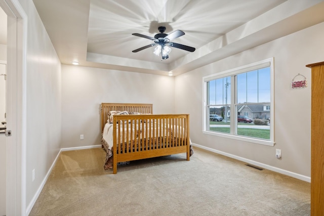 carpeted bedroom with ceiling fan and a tray ceiling