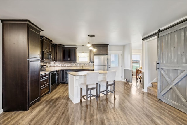 kitchen featuring appliances with stainless steel finishes, hanging light fixtures, backsplash, a center island, and a barn door