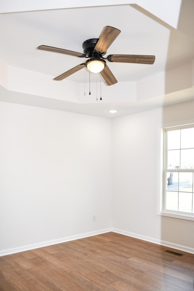 unfurnished room with hardwood / wood-style floors, a tray ceiling, and ceiling fan