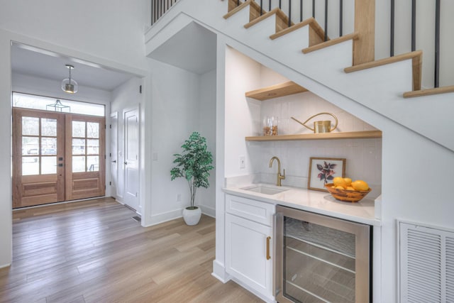 bar featuring french doors, sink, white cabinetry, beverage cooler, and light hardwood / wood-style floors