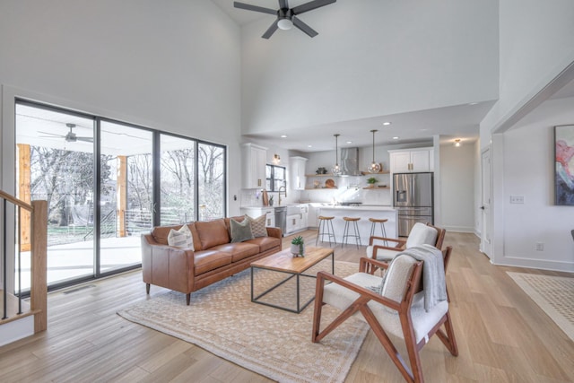 living room featuring ceiling fan, a towering ceiling, and light hardwood / wood-style flooring