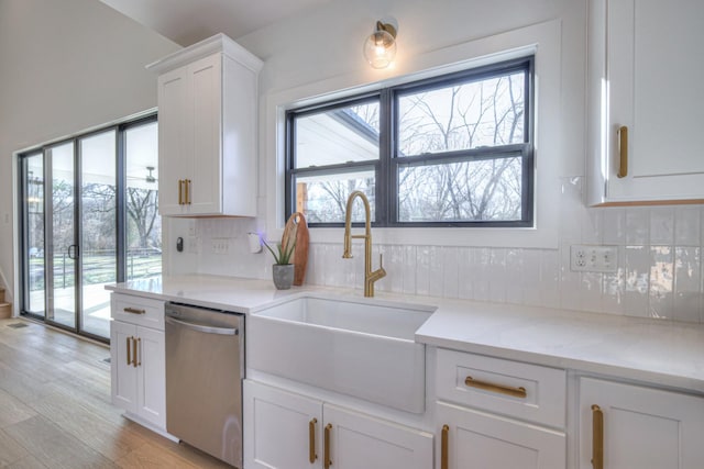 kitchen with sink, white cabinets, stainless steel dishwasher, light stone countertops, and light wood-type flooring