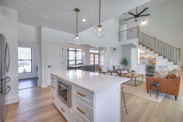 kitchen with appliances with stainless steel finishes, white cabinetry, hanging light fixtures, a kitchen island, and beverage cooler