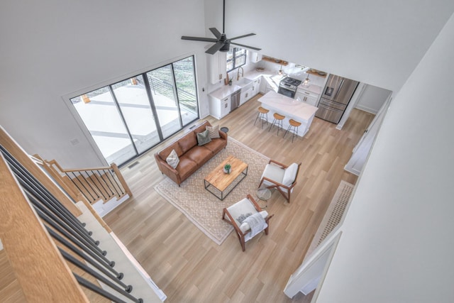 living room with ceiling fan, light hardwood / wood-style flooring, and a towering ceiling