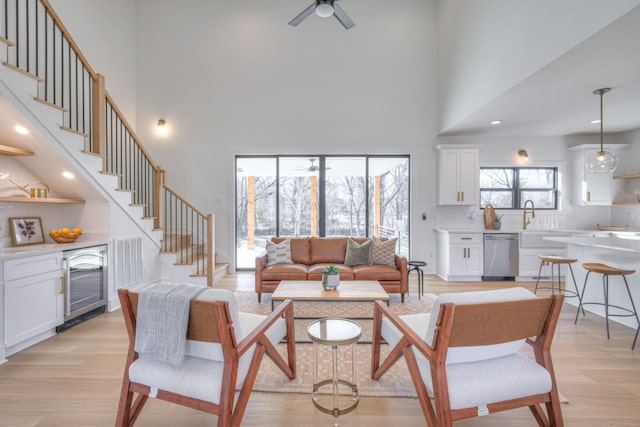 living room with a high ceiling, ceiling fan, beverage cooler, and light wood-type flooring