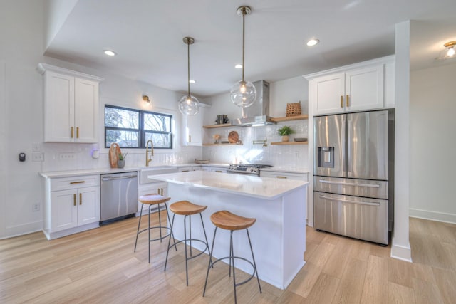 kitchen with wall chimney range hood, stainless steel appliances, a center island, and white cabinets