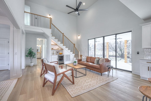 living room with a towering ceiling, beverage cooler, ceiling fan, bar area, and light wood-type flooring