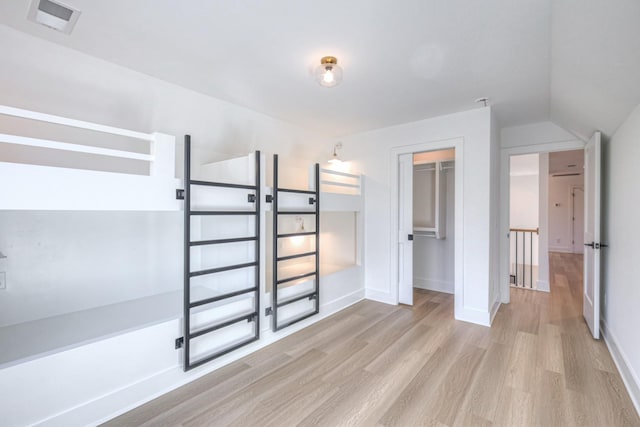 unfurnished bedroom featuring lofted ceiling, a closet, and light wood-type flooring