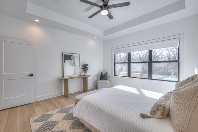 bedroom with ceiling fan, a tray ceiling, and light hardwood / wood-style floors