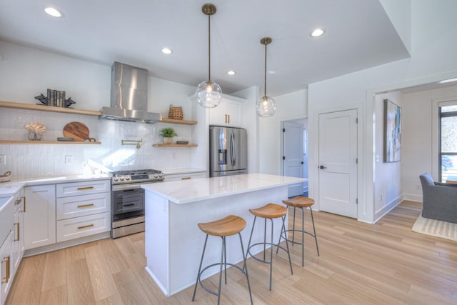 kitchen featuring white cabinetry, wall chimney exhaust hood, stainless steel appliances, and a kitchen island