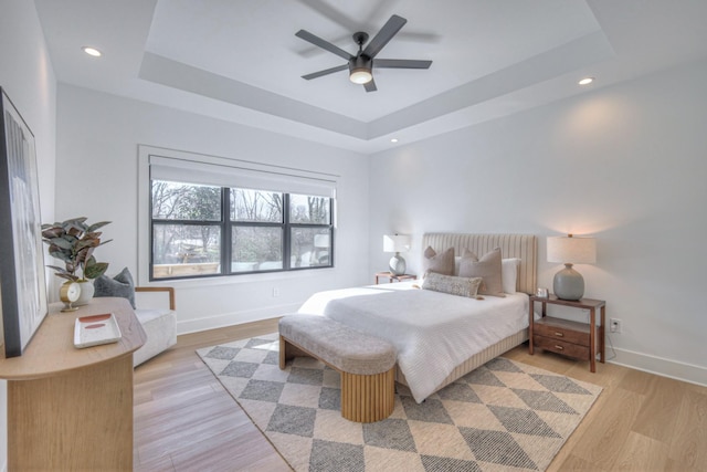 bedroom featuring light hardwood / wood-style floors, ceiling fan, and a tray ceiling