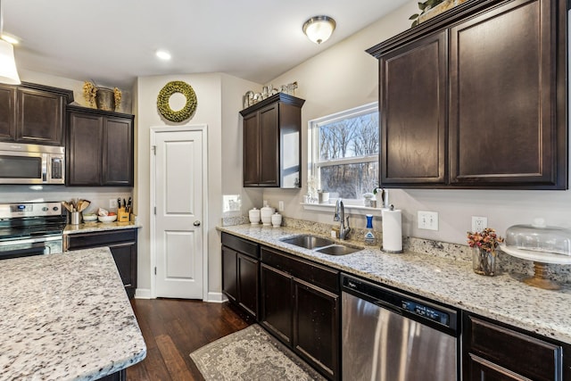 kitchen with sink, appliances with stainless steel finishes, dark hardwood / wood-style floors, dark brown cabinetry, and light stone counters