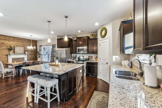 kitchen featuring a kitchen island, decorative light fixtures, wood walls, sink, and stainless steel appliances