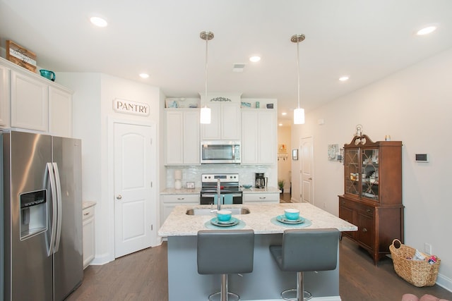 kitchen featuring white cabinetry, hanging light fixtures, appliances with stainless steel finishes, an island with sink, and light stone countertops